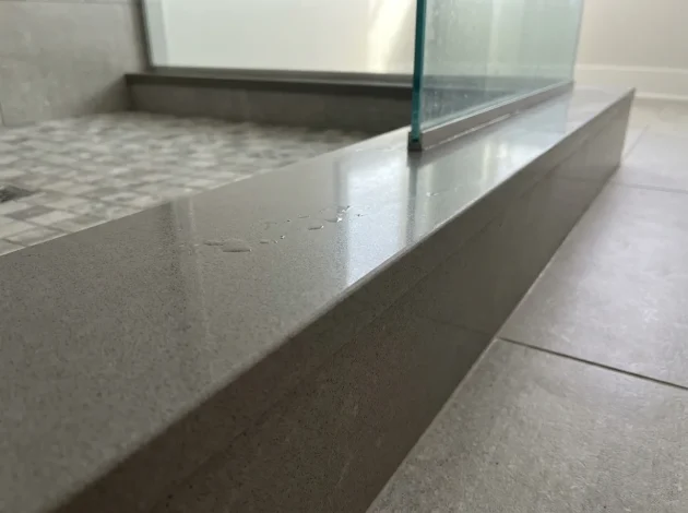 Grey Caesarstone threshold used as a shower curb in a walk-in shower