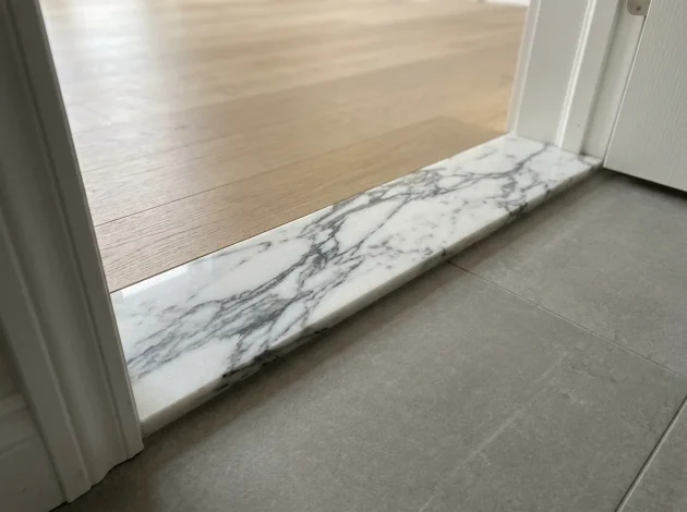 Statuario Marble threshold installed in a doorway between hardwood and tile flooring