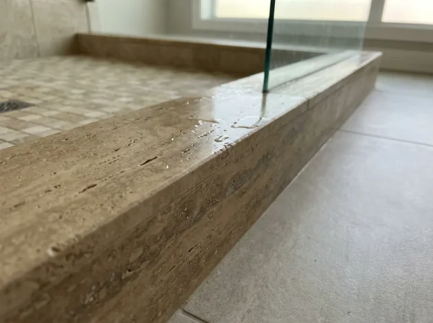 Umbral de travertino utilizado como bordillo de ducha en una ducha a ras de suelo
