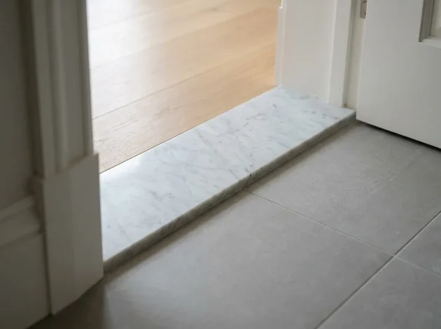 Umbral de mármol blanco de Carrara instalado en una puerta entre pisos de madera y baldosas